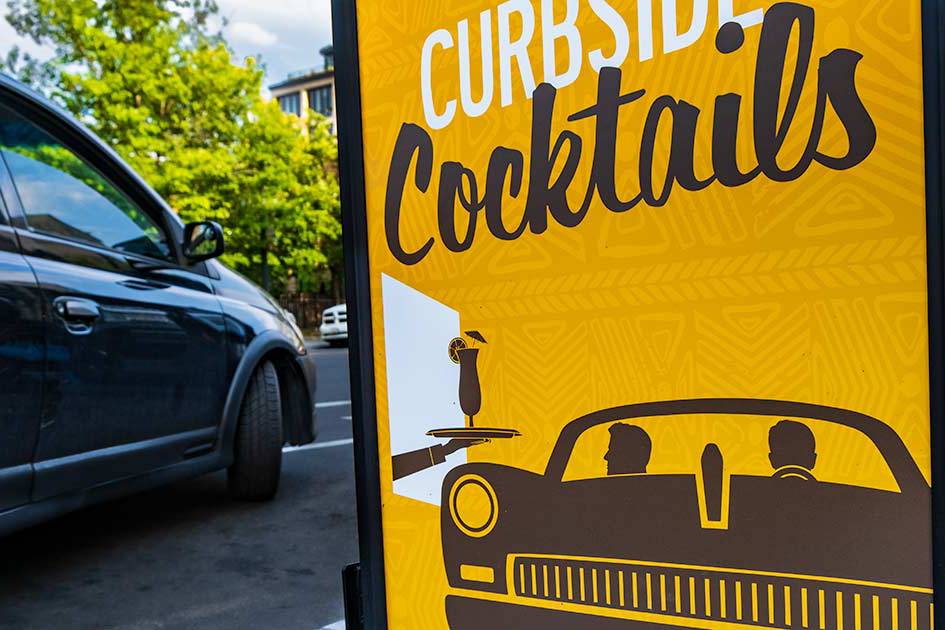 Curbside cocktails sign with a car parked beside it