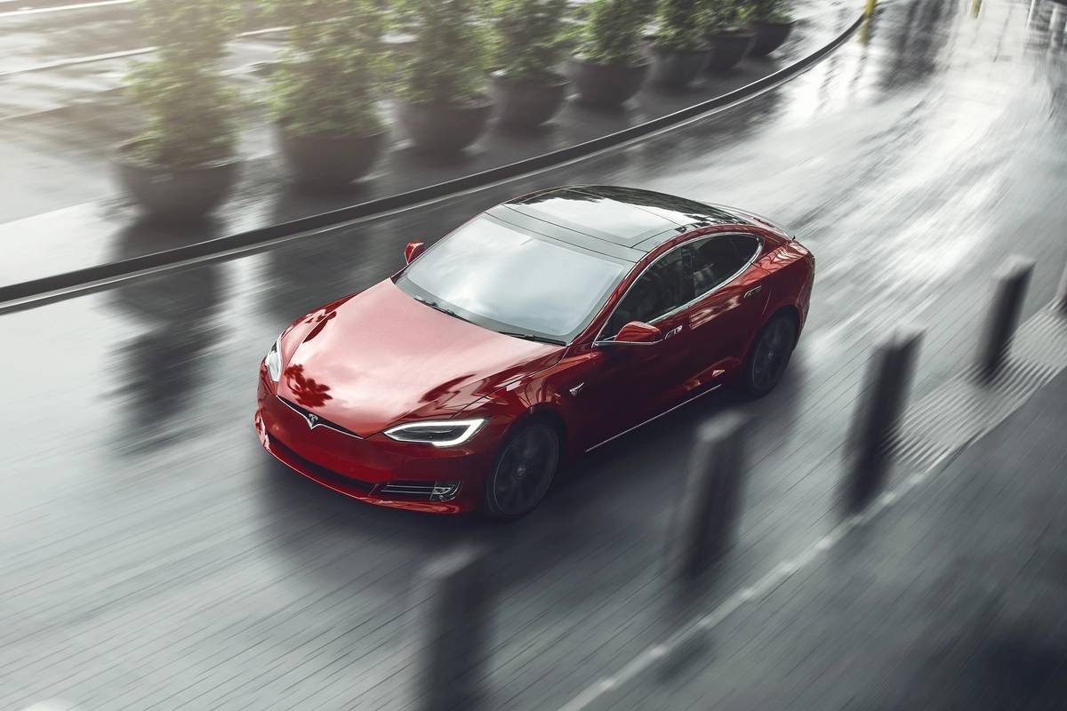 A red Tesla Model S driving on a wet road